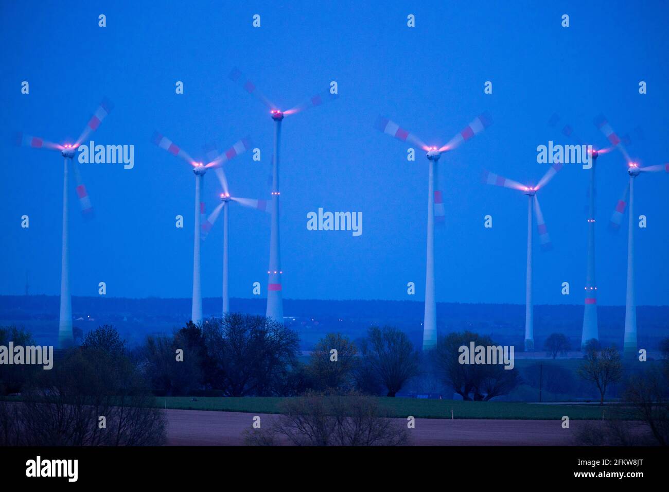 Pasewalk, Deutschland. April 2021. Beleuchtete Windenergieanlagen rotieren in einem Windpark nach Sonnenuntergang. Nach dem Urteil des Bundesverfassungsgerichts zum Klimaschutzkonzept fordert das Umweltbundesamt (UBA) einen schnelleren Ausbau der Windenergie. Quelle: Jens Büttner/dpa-Zentralbild/dpa/Alamy Live News Stockfoto