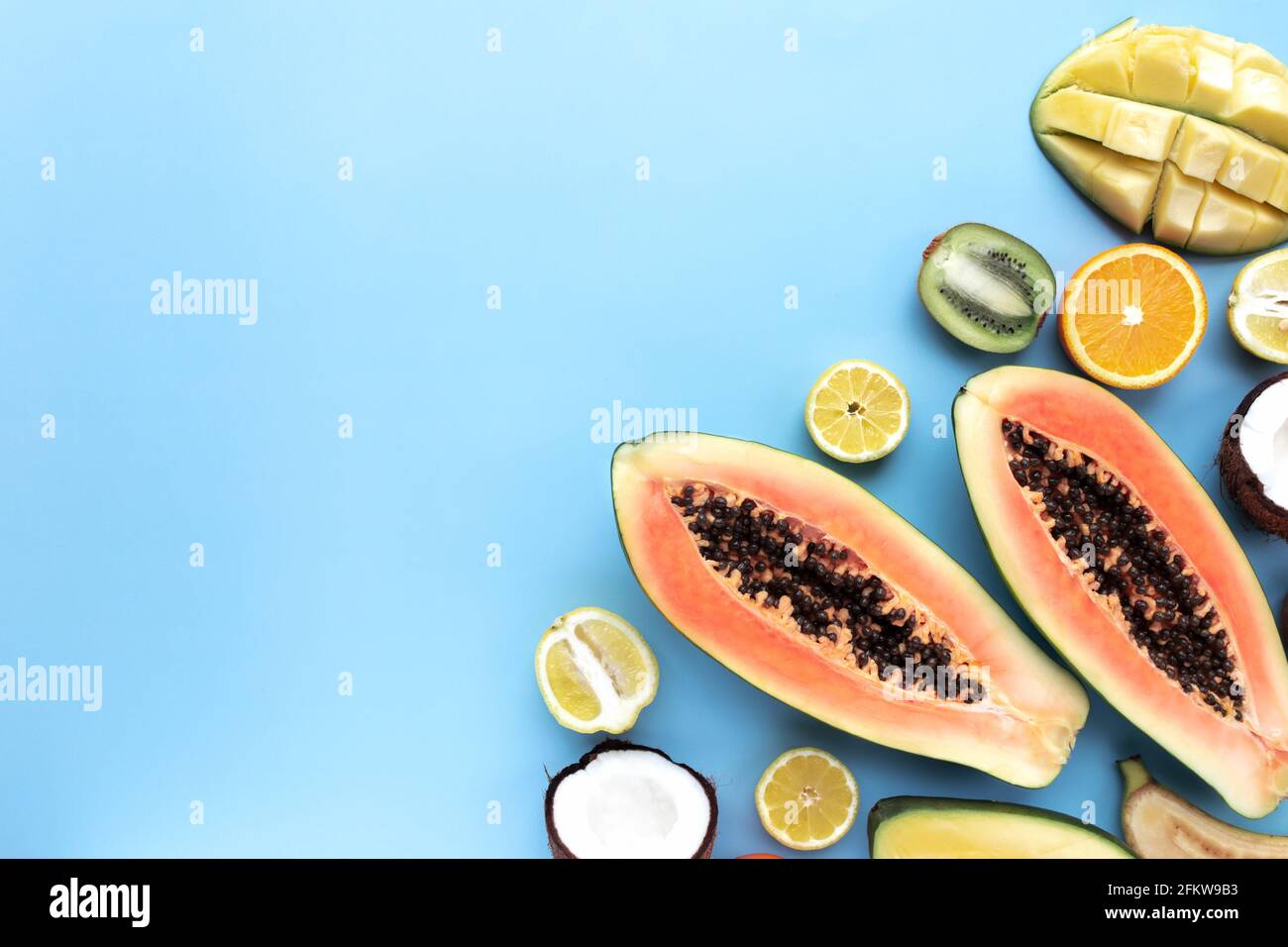 Verschiedene frische, tropische Schnittfrüchte auf blauem Hintergrund. Papaya, Orange, Banane, Kokosnuss, Mango, Kiwi und Zitrone Draufsicht flach Lay mit Kopieplatz für Stockfoto