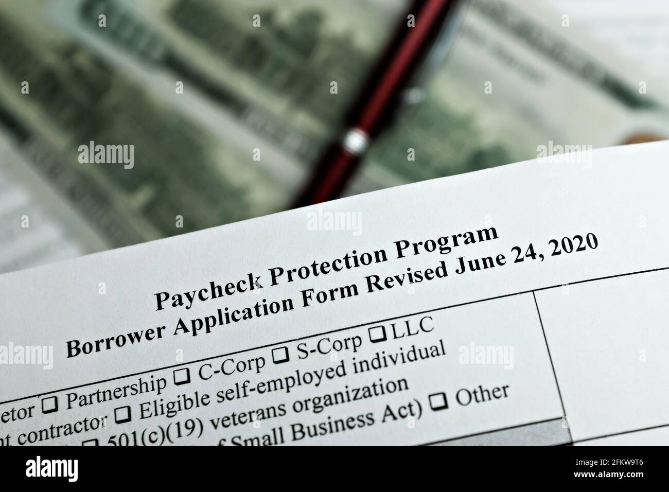 Selektive Fokus Foto von Gehaltsscheck Schutz Programm Kreditnehmer Antragsformular überarbeitet, auf einem Hintergrund von Dollar-Scheine und einen Stift Stockfoto