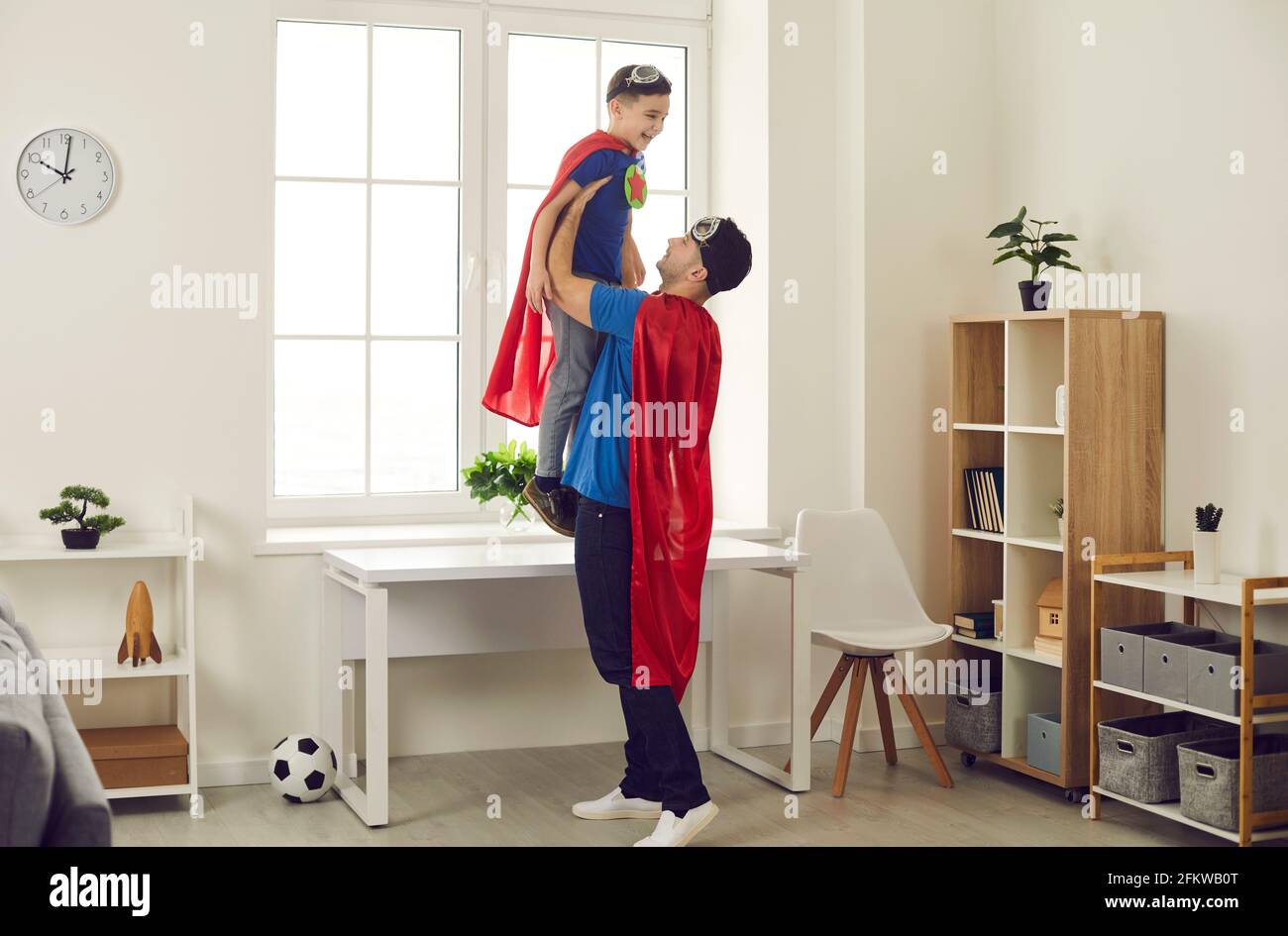 Glücklicher Vater und lustiger kleiner Sohn in Superhelden-Umhänge Spielen Sie lustige Spiele zu Hause Stockfoto