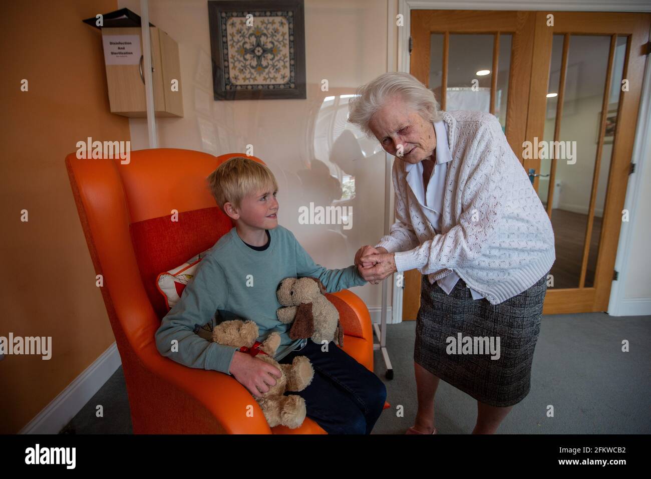 Eine ältere Frau in den Achtzigern mit Demenz hält ihren Enkel in einem Pflegeheim in England, Großbritannien, in der Hand Stockfoto