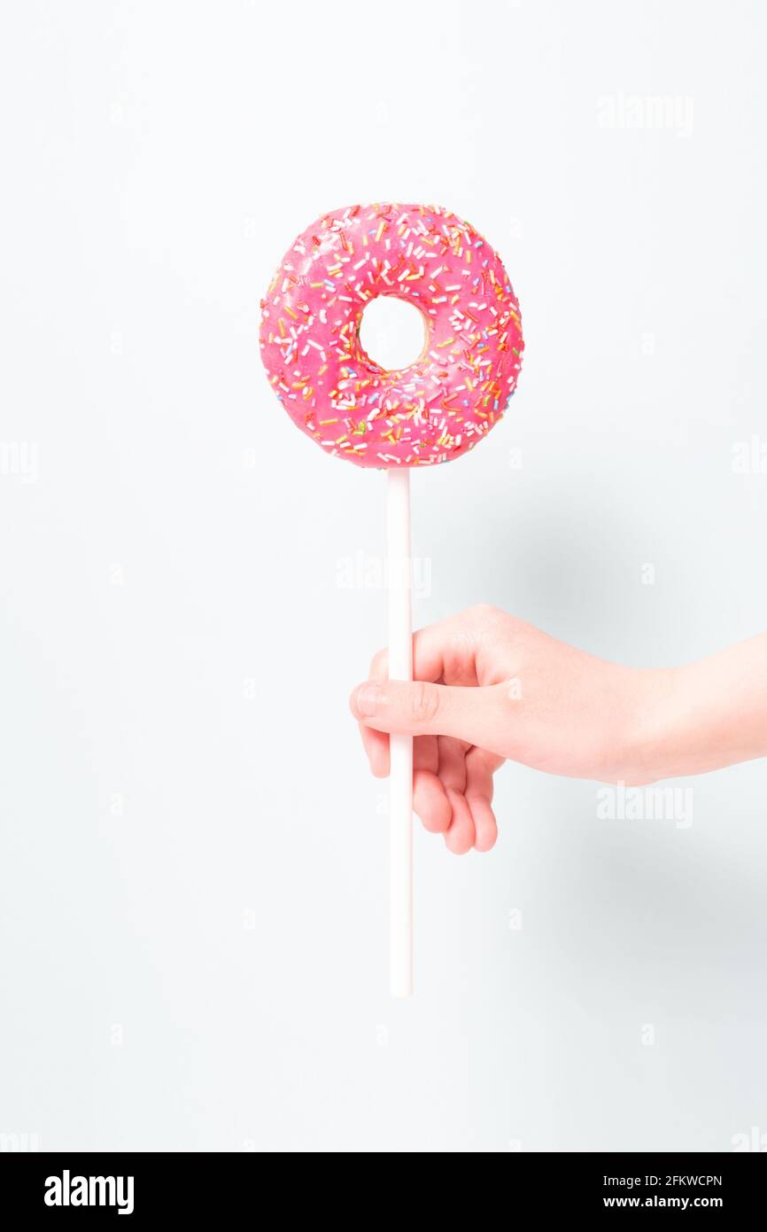 Lustig lecker rosa Donut auf Stick in der Hand des Kindes wie Lollipop. Minimalismus. Donut-Tag. Stockfoto Lustig lecker rosa Donut auf Stick in der Hand des Kindes wie Lollipop. Minimalismus. Donut-Tag. Stockfoto