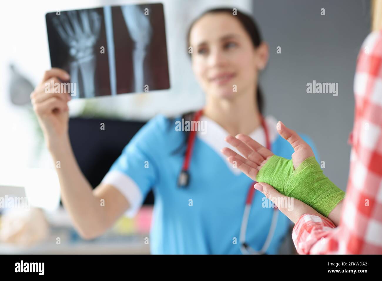 Der Arzt untersucht die Röntgenaufnahme der Hand neben dem stehenden Patienten Mit bandageter Hand Stockfoto