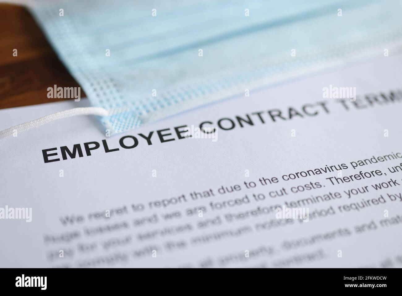 Die Kündigung des Arbeitsvertrags aufgrund einer Coronavirus-Pandemie sowie eine Schutzmaske liegen auf dem Tisch Stockfoto