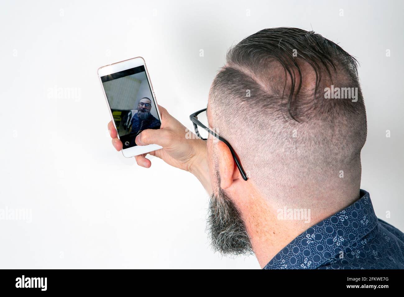 Bärtiger Hipster, der sein Smartphone benutzte, um ein Selfie zu machen, von hinten gesehen und auf dem Handy reflektiert Stockfoto