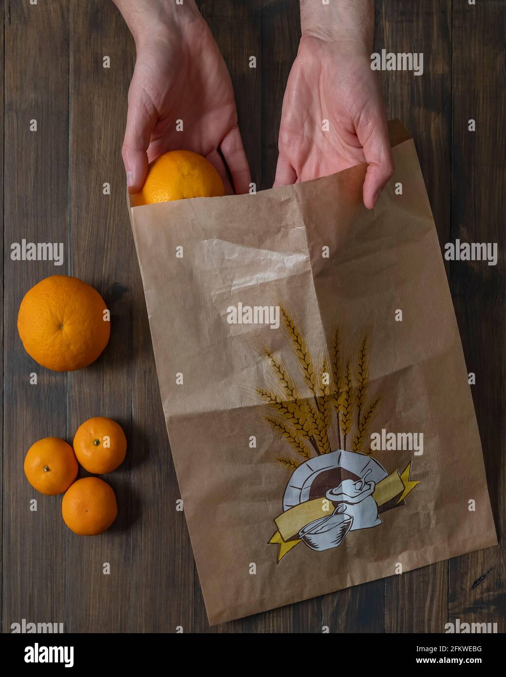 Handflächen aus männlichen Händen halten eine Orange und einen Papierbeutel, um den Schutz des Planeten mit umweltfreundlichen Materialien und Null-Kilometer-Produkten zu repräsentieren Stockfoto