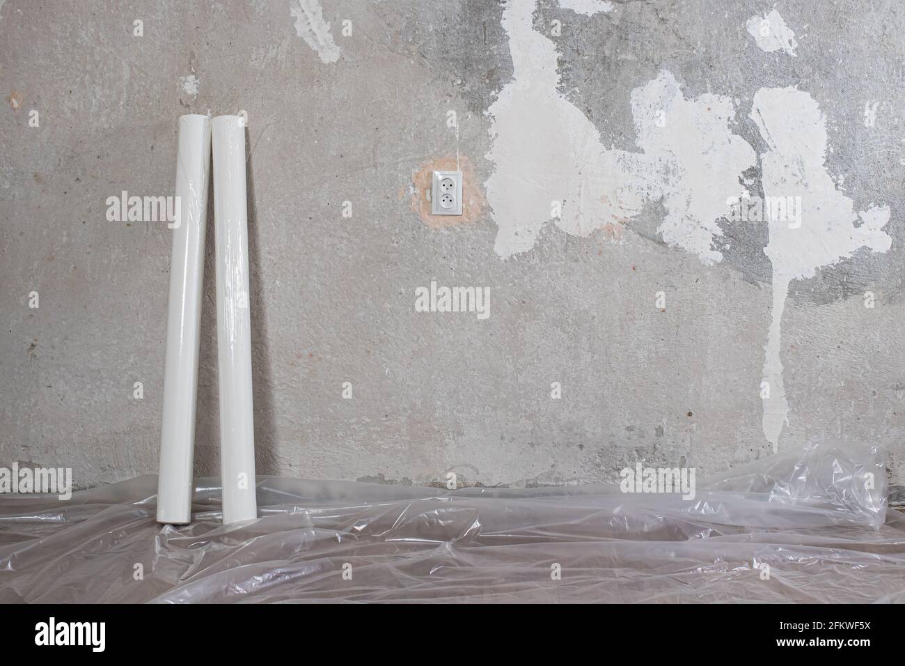 Der Raum befindet sich in einem Zustand der Reparatur - 2 Rollen weißer Tapete, eine alte Betonwand mit Spuren von Gips und ein Auslass. Renovierung des Hauses mit Stockfoto