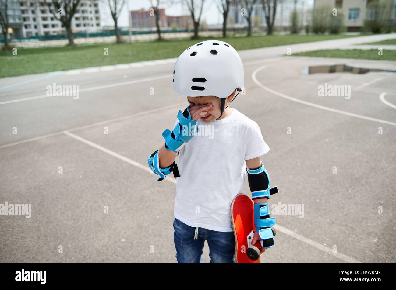 Verärgert Junge Skateboarder in Schutzkleidung frustriert wischt Tränen aus  Seine Augen und hält ein Skateboard in einer Hand, während Auf einem  Sportspieler stehen Stockfotografie - Alamy