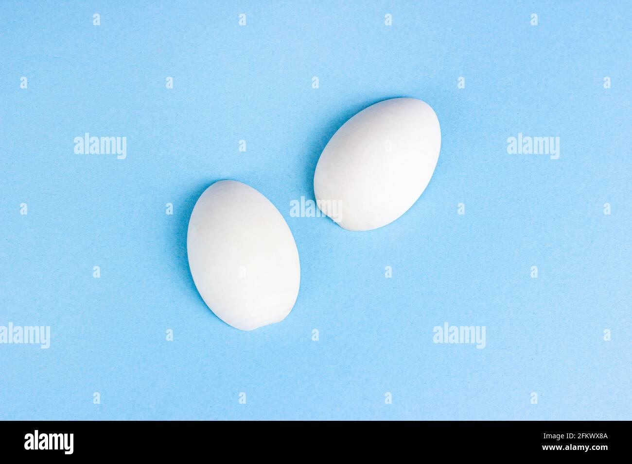 Zwei weiße Holzeier auf hellblauem Hintergrund. Stockfoto