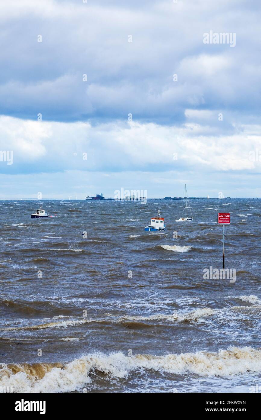 Kleine Boote bei Anchor reiten auf den Wellen bei unsaisonalen Stürmen Anfang Mai an der Themse-Mündung mit Southend Pier Hintergrund Stockfoto