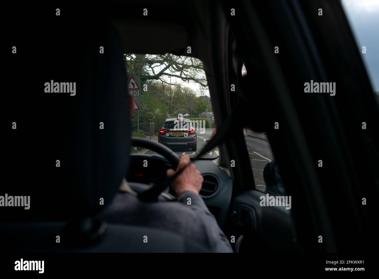 Ein älterer Autofahrer folgt einem lernenden Fahrer, der vom Rücksitz hinter dem Fahrer aus gesehen wird. Stockfoto