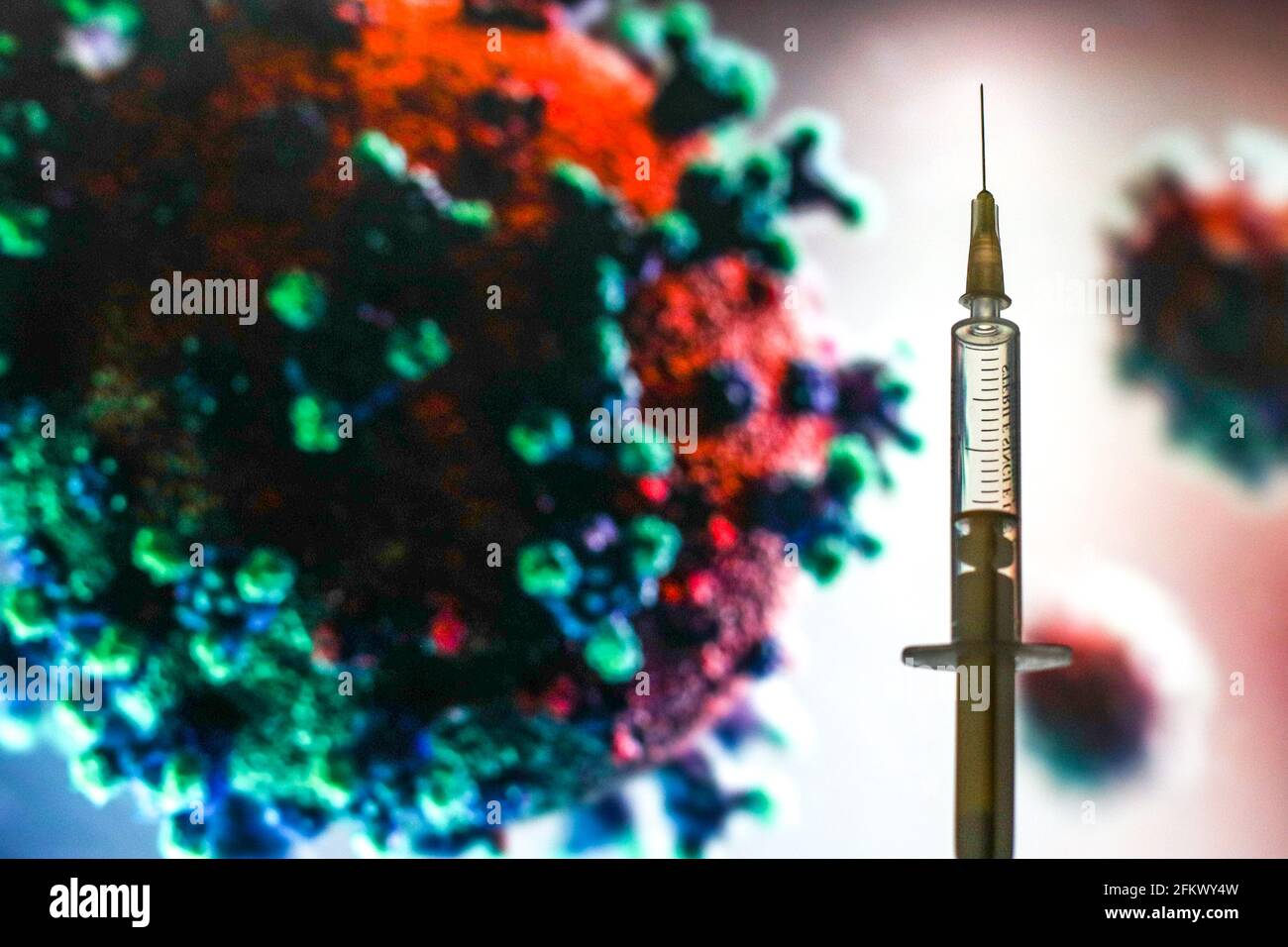 In dieser Abbildung ist eine medizinische Spritze vor einem mikroskopischen Bild des Coronavirus zu sehen. Stockfoto