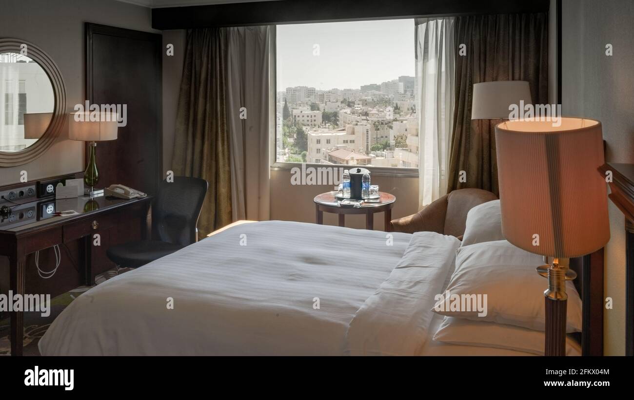 Frisch zubereitetes Kingsize-Bett in einem gemütlichen Hotelzimmer mit Blick auf Amman, Jordanien an einem klaren Tag Stockfoto