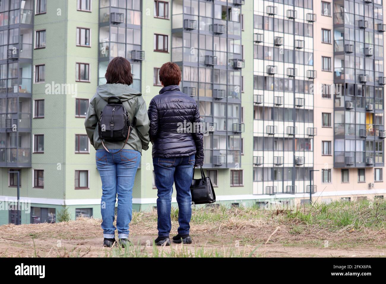 Zwei Frauen schauen sich die auf einem Hügel stehenden Hochhäuser an. Auswahl und Kauf einer Wohnung, Bau von Wohngebäuden und Immobilien Stockfoto