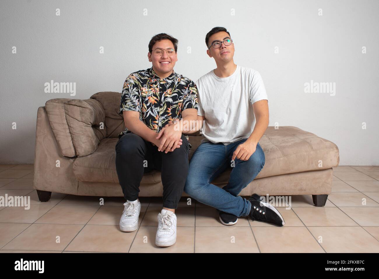 Männliches Paar, das in ihrem leeren Wohnzimmer sitzt, schaut glücklich Am Horizont Stockfoto