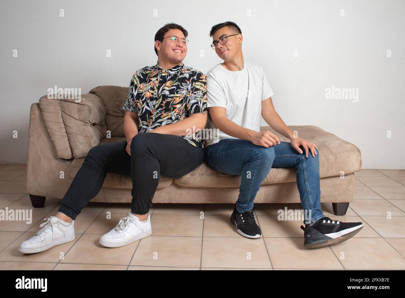 Männliches Paar, das in ihrem leeren Wohnzimmer sitzt, schaut glücklich Am Horizont Stockfoto