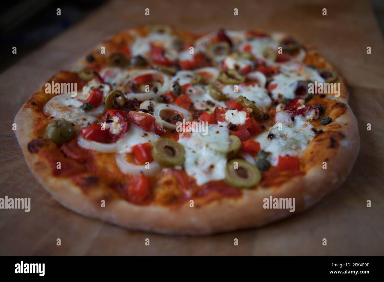 Hausgemachte Pizza frisch aus dem Ofen. Tomatenbasis mit roten Paprika, Zwiebeln, grünen Oliven, Kapern und Büffelmozzarella gekrönt Stockfoto