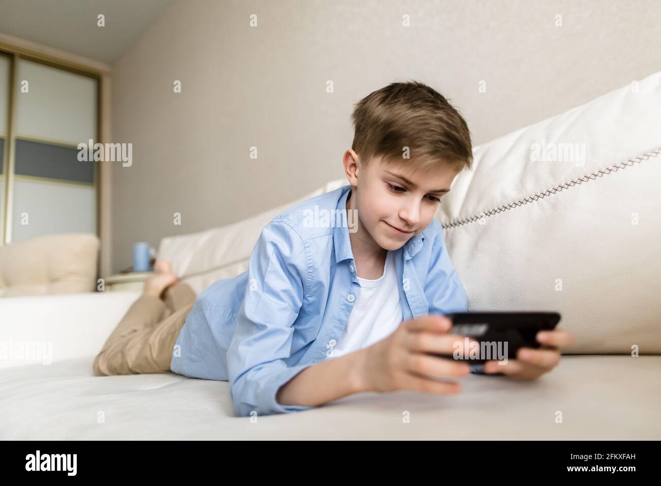 Kind liegt in den Händen auf der Couch und hält ein Telefon, spielt mit ihm. Stockfoto