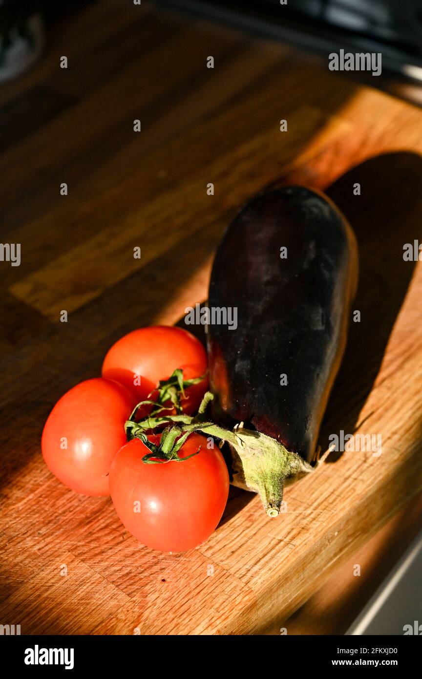 Tomaten auf der Rebe und eine frische Aubergine (Aubergine) Solanum Melongena auf einem Holzbrett Stockfoto