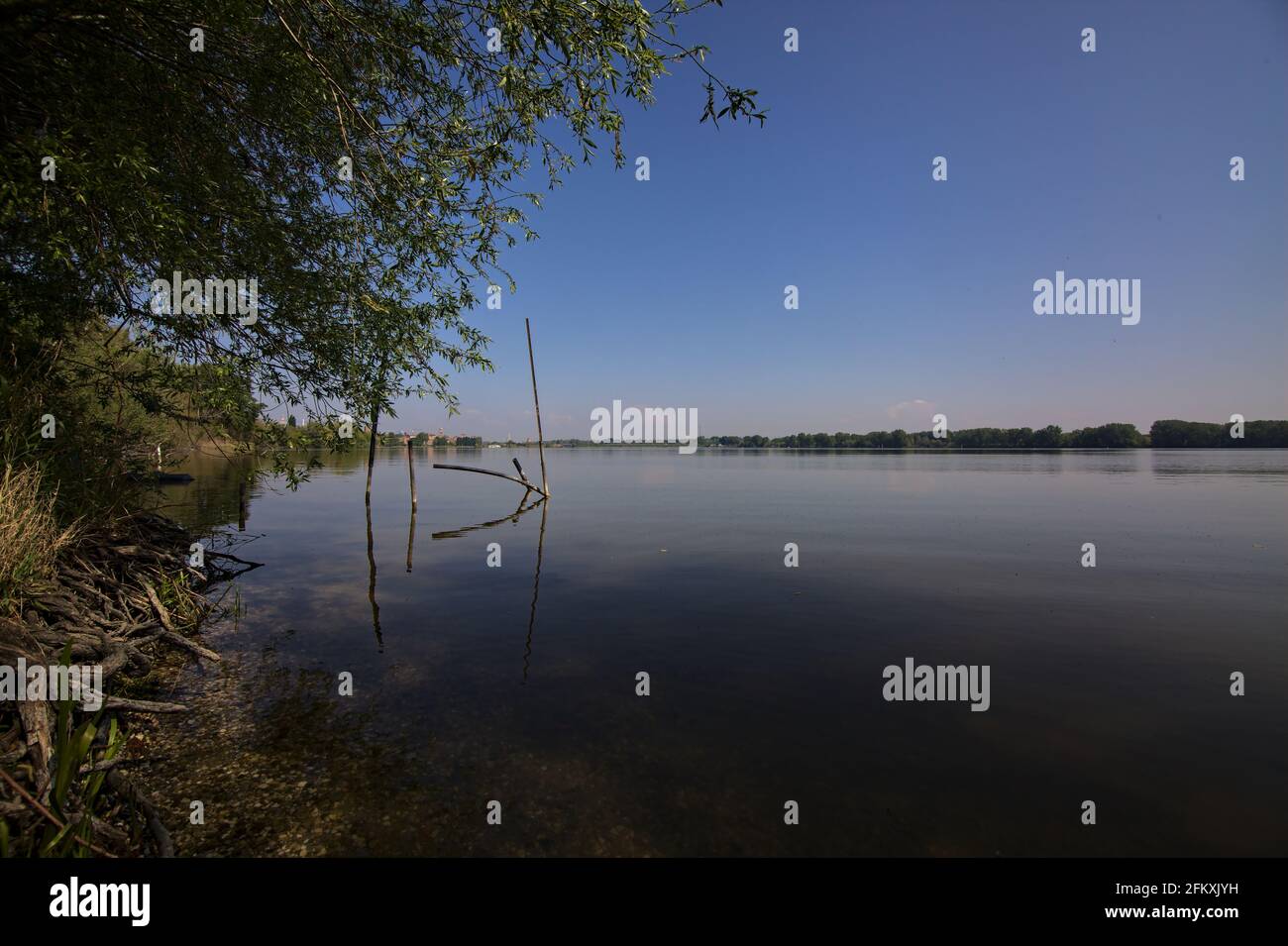 See mit einer Fabrik in der Ferne eingerahmt von der Laub von Bäumen in der italienischen Landschaft Stockfoto