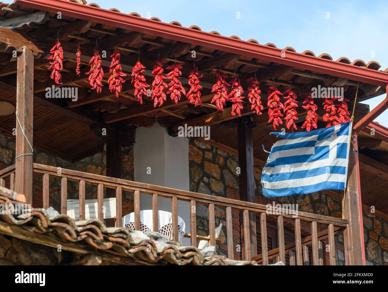 Chilischoten trocknen und eine griechische Flagge fliegen, auf dem Balkon eines Hauses im Fischerdorf Psarades am Prespa-See, Mazedonien, Nord-Greec Stockfoto