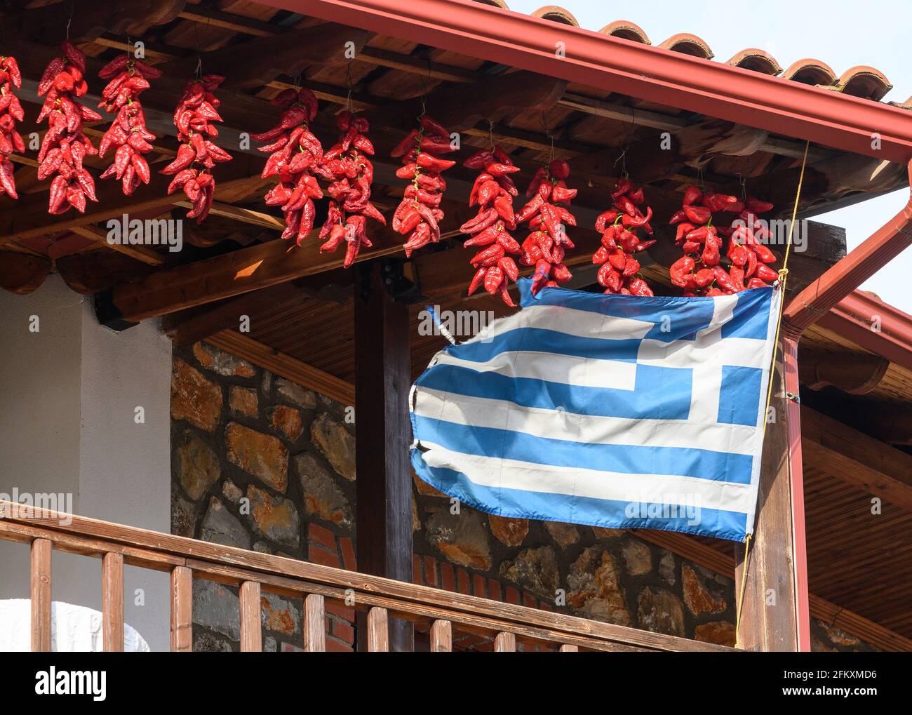 Chilischoten trocknen und eine griechische Flagge fliegen, auf dem Balkon eines Hauses im Fischerdorf Psarades am Prespa-See, Mazedonien, Nord-Greec Stockfoto