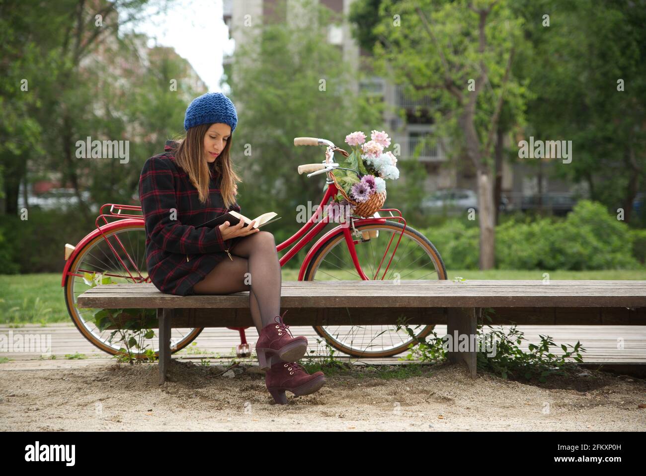 Frau liest ein Buch, ein rotes Fahrrad und einen Korb mit bunten Blumen. Stockfoto