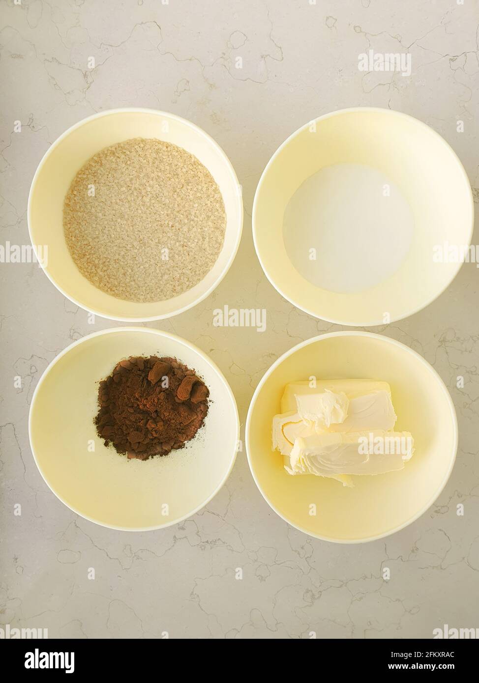 4 Schüsseln mit Zutaten Zucker Kakaobutter Milch Marmortisch Flach liegend Stockfoto