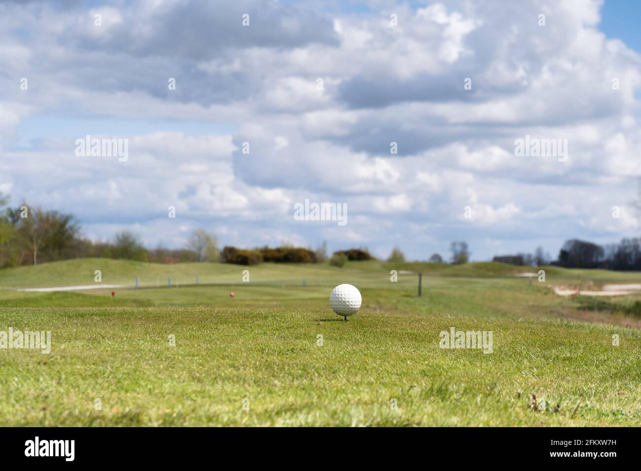 Weißer Golfball auf einem Abschlag auf einem Golfplatz mit schönem bewölktem Himmel darüber. Konzentrieren Sie sich auf den Golfball, geringe Schärfentiefe Stockfoto