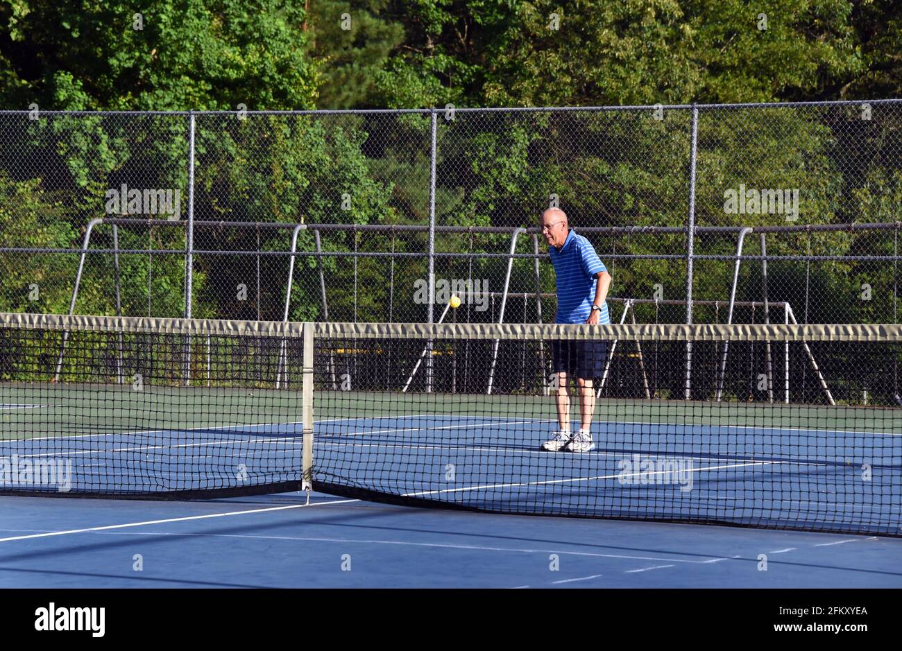 Pickle Ball springt in die Luft und älterer Mann schwingt. Er spielt auf einem Tennisplatz. Stockfoto