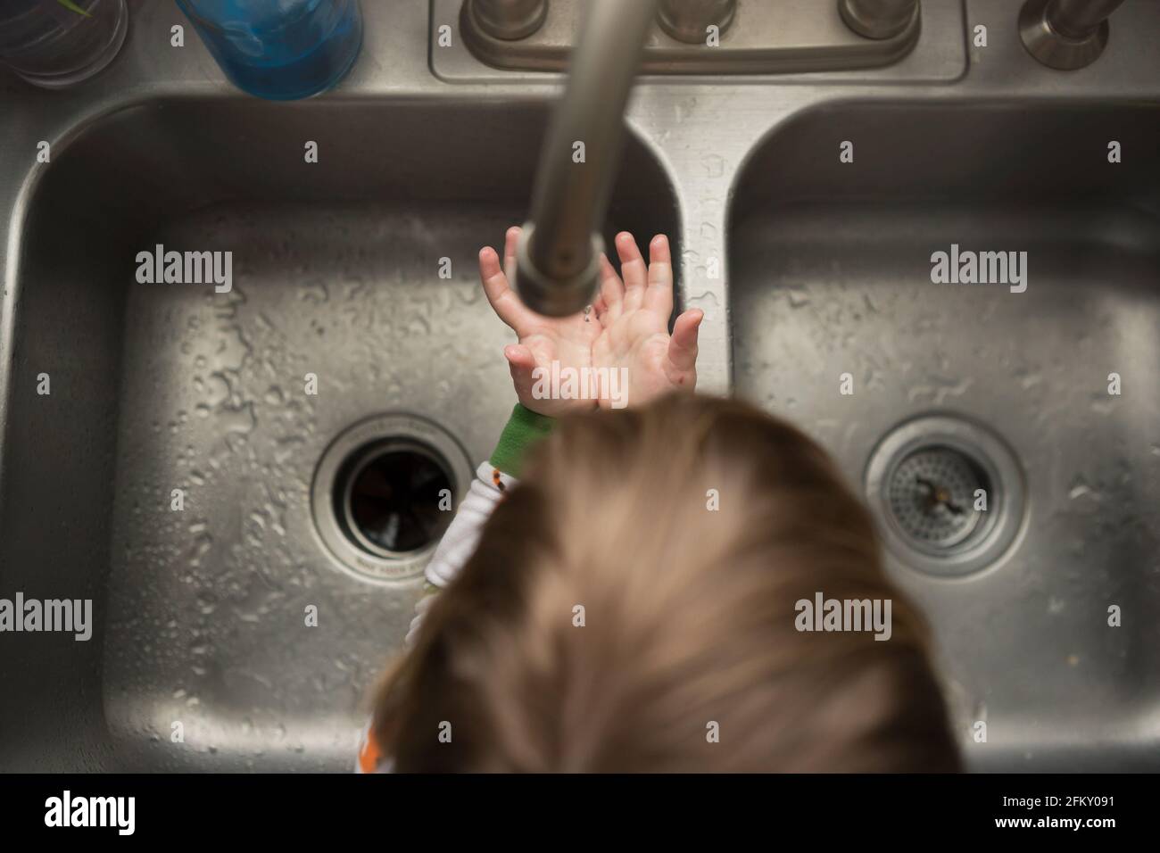 Das Kleinkind hält die Hände aus der Küche, um zu spüren, wie Wasser aus der Küche tropft Waschbecken Stockfoto