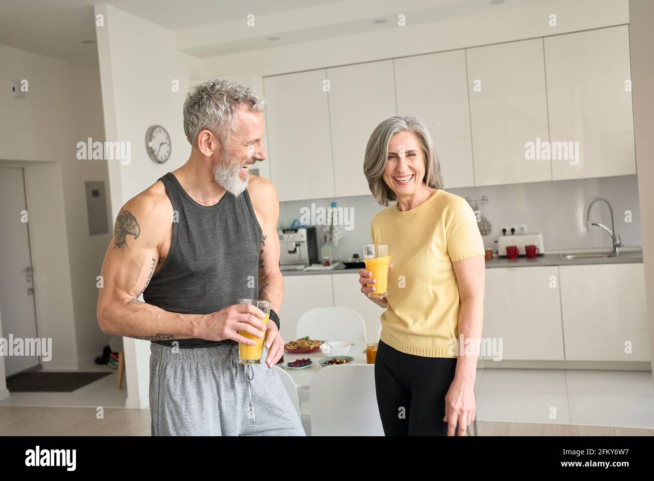 Gesundes sportlich glückliches Seniorenpaar trinkt Saft und lacht zu Hause. Stockfoto