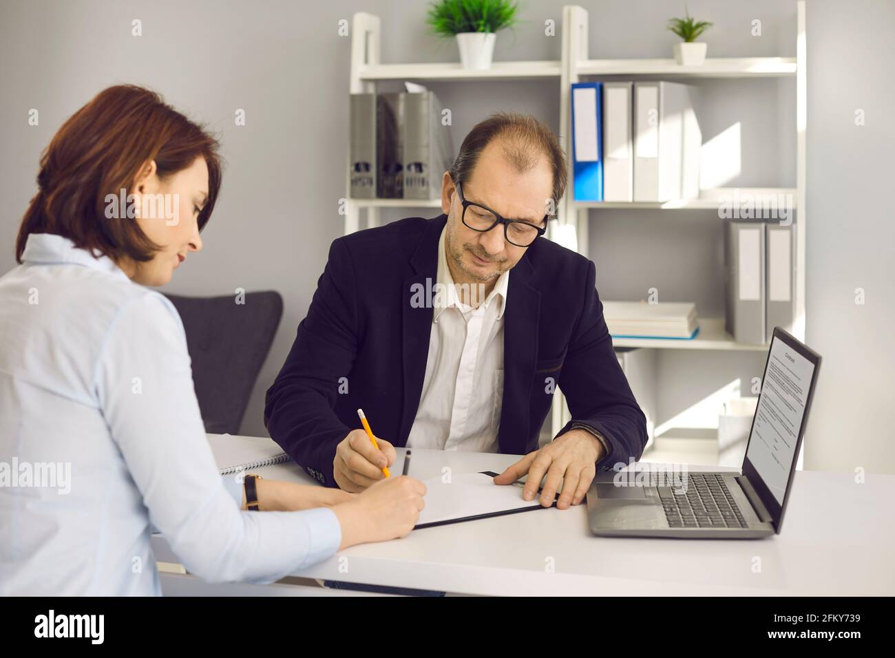 Eine Frau bei einem Treffen in der Bank unterschreibt ein Dokument, das im Büro an einem Tisch mit einem Manager sitzt. Stockfoto