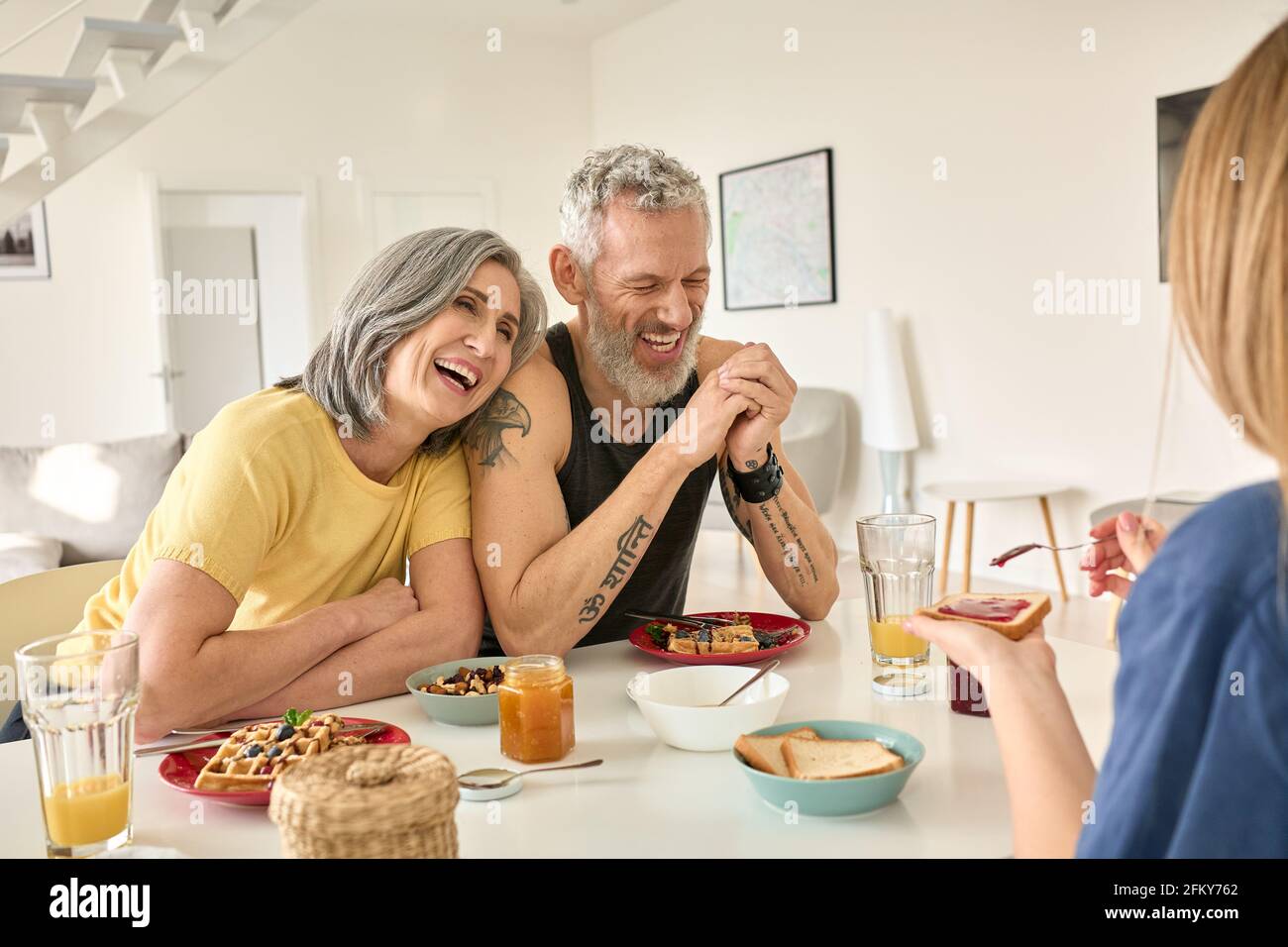 Glückliches reifes Familienpaar beim Frühstück mit Tochter sitzen am Küchentisch. Stockfoto