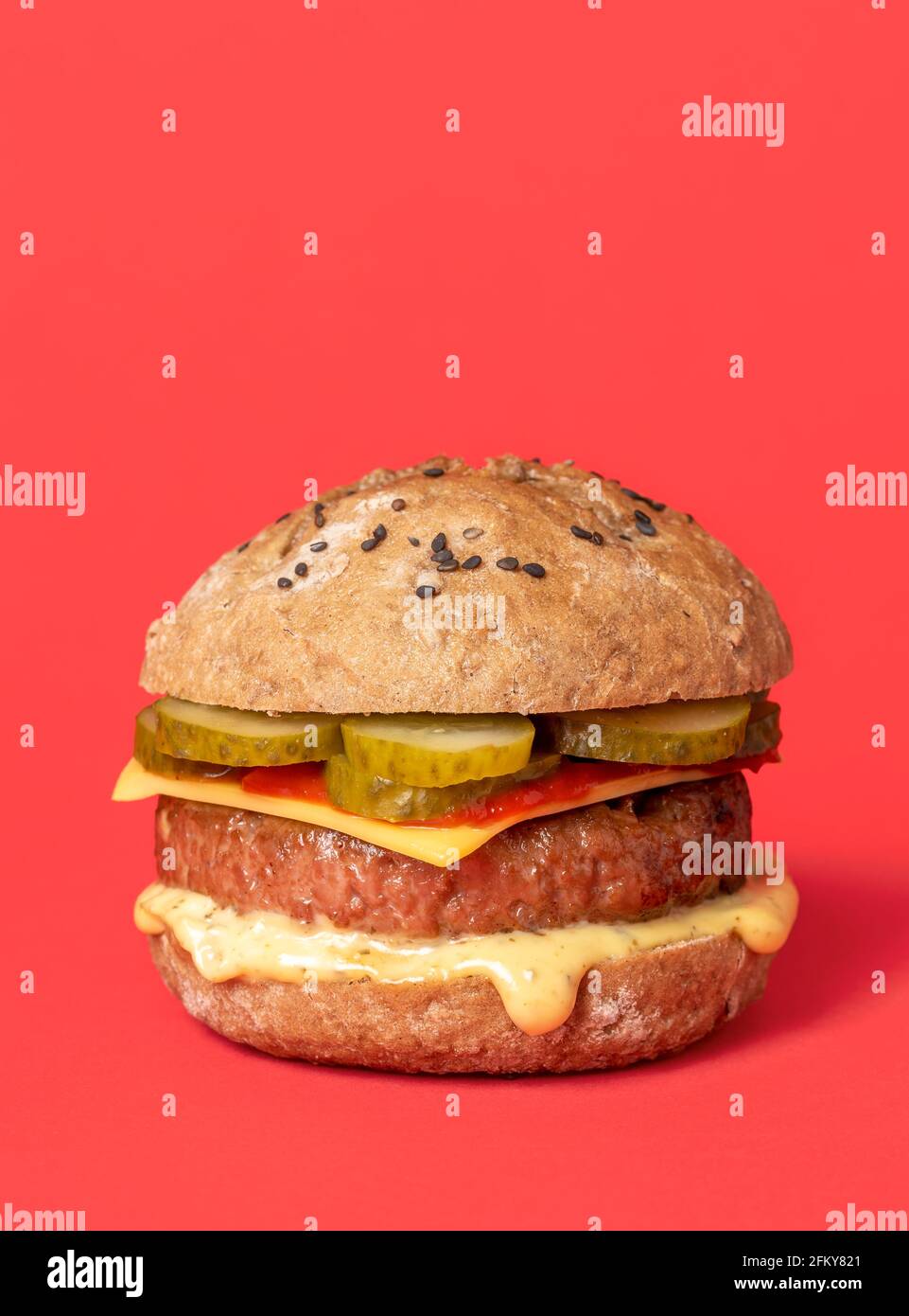 Hausgemachter veganer Burger mit Sojapastete, Cashew-Käse und veganen Saucen. Burger auf pflanzlicher Basis auf einem roten Hintergrund isoliert. Stockfoto