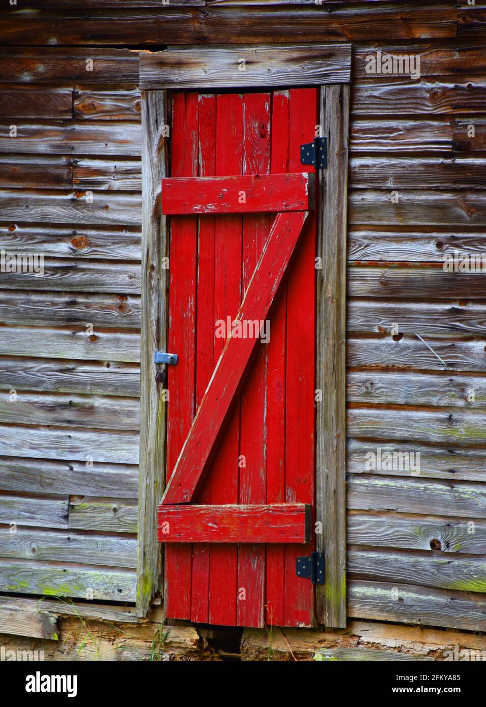 Rustikale, hölzerne, verwitterte Scheune Tür ist leuchtend rot lackiert. Der Bau beginnt zu verrotten und Bretter sind reparaturbedürftig. Bretter bilden den Buchstaben z. Stockfoto