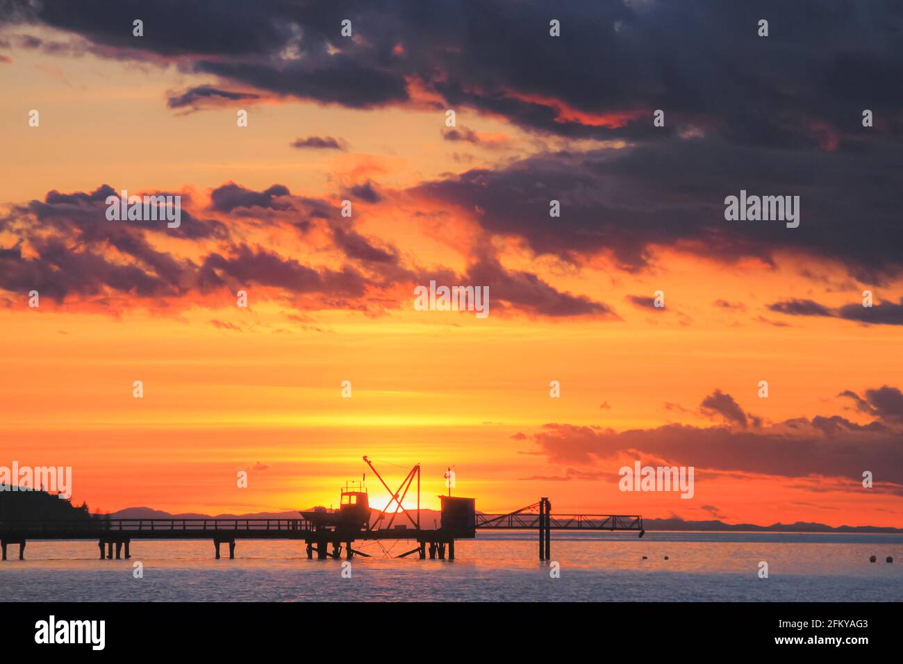 Moody, dramatisch, farbenfroh und lebhaft orange Sonnenuntergang oder Sonnenaufgang Himmel über Burrard Inlet Pier am Kitsilano Beach in Vancouver, British Columbia, Kanada Stockfoto