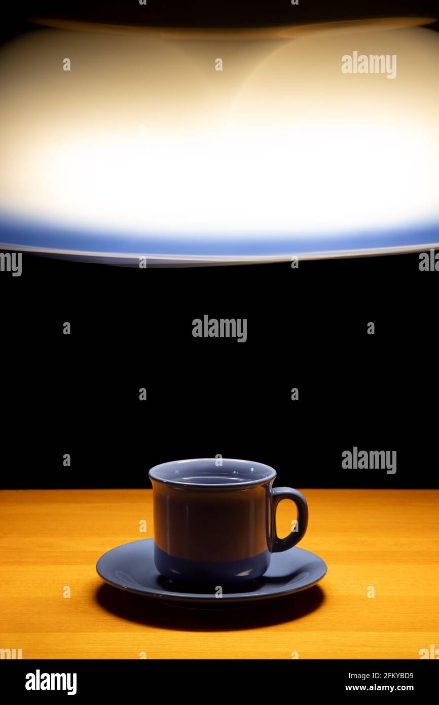 Eine Teetasse auf dem Tisch unter einem beweglichen Kronleuchter auf schwarzem Hintergrund Stockfoto