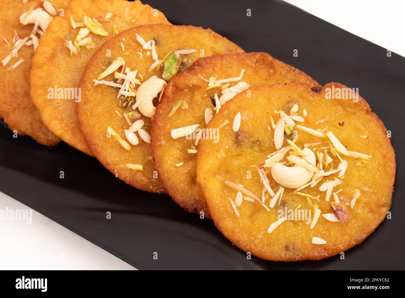 Stacked Indian Delight Mawa Malpua Mithai In Cheeni Ki Getränkt Chashni oder Chaashni und arrangiert auf schwarzem Tablett verziert mit Trockene Früchte Pistazien Pi Stockfoto