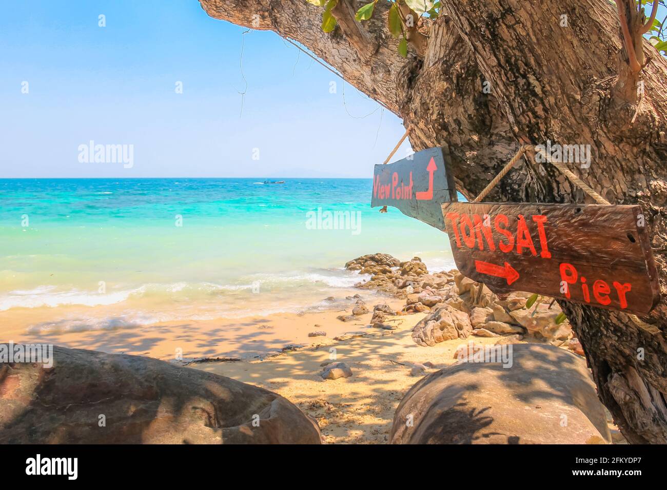 Idyllisches, tropisch blaues, türkisfarbenes Wasserwasser am Loh Moo Dee Beach mit hölzernen Touristenschildern zum Aussichtspunkt und zum Tonsai Pier auf Koh Phi Phi, Thailan Stockfoto