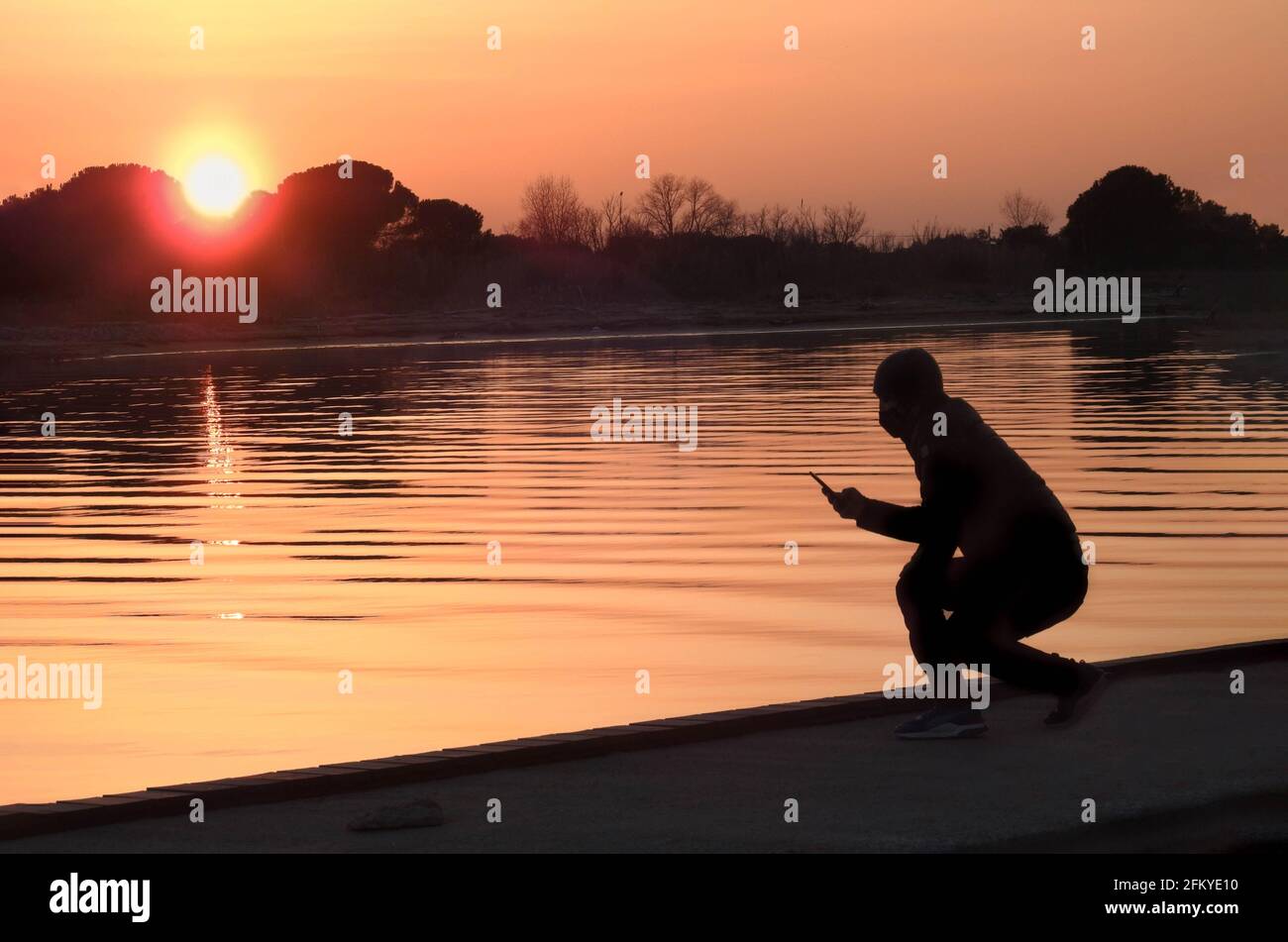 Kerl mit Smartphone in der Hand bei Sonnenuntergang auf dem Fluss Stockfoto