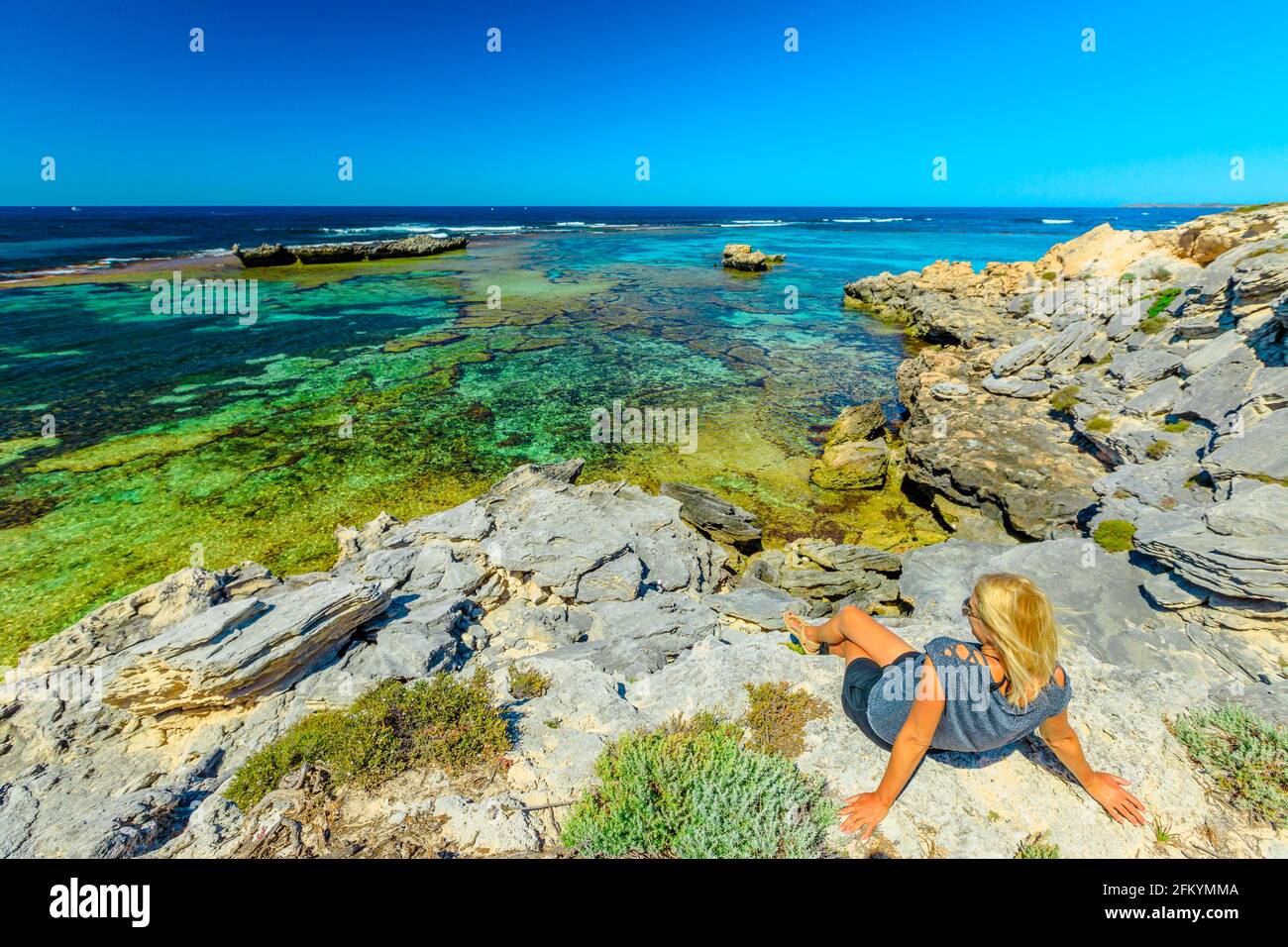 Kaukasisches Touristenmädchen sonnen sich auf Felsen, das türkisfarbene Wasser des Jeannies Lookout auf Rottnest Island, Perth, Westaustralien. Panoramablick Stockfoto