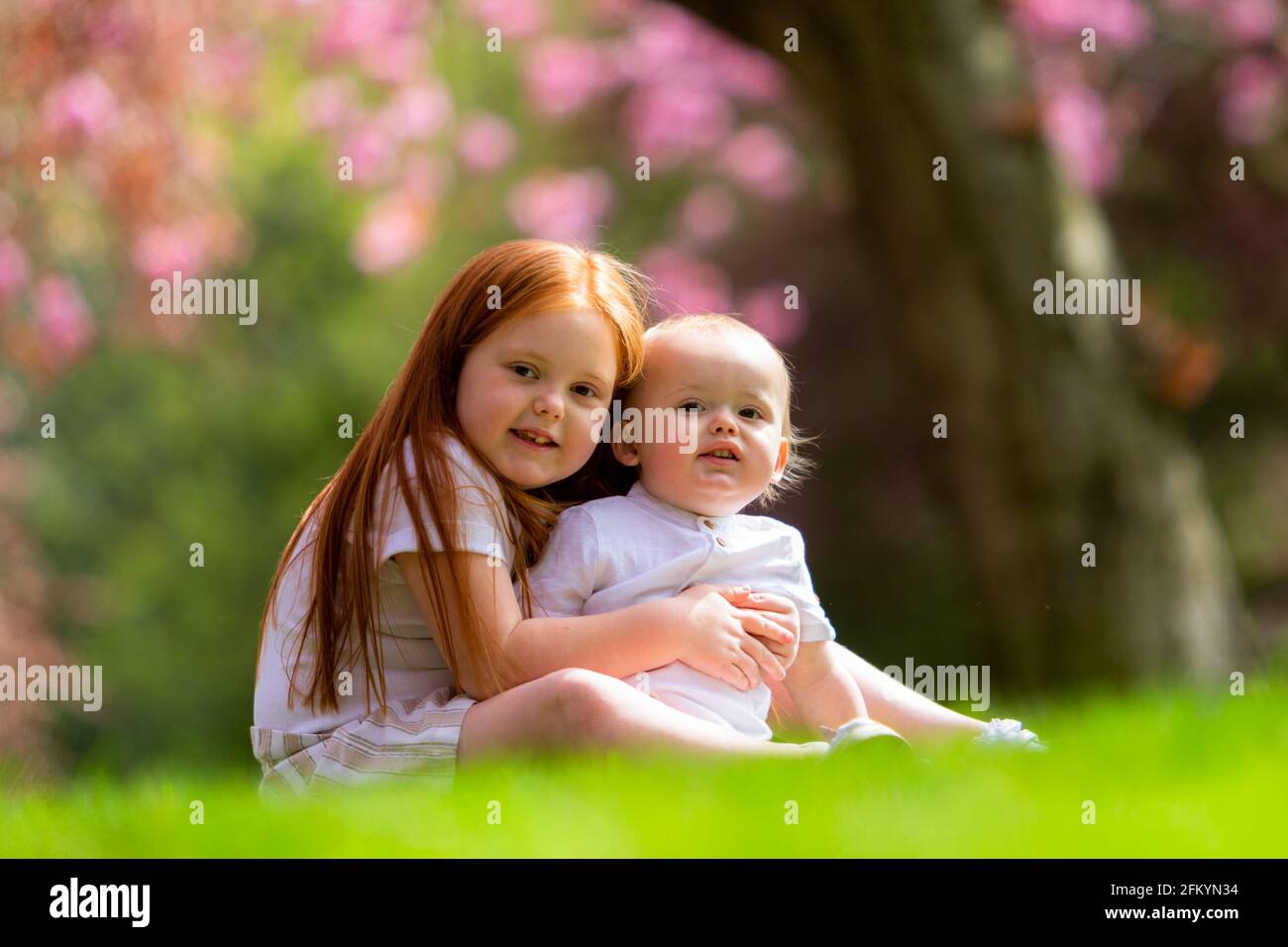 Junges Mädchen mit ihrem kleinen Bruder draußen auf der Gras Stockfoto