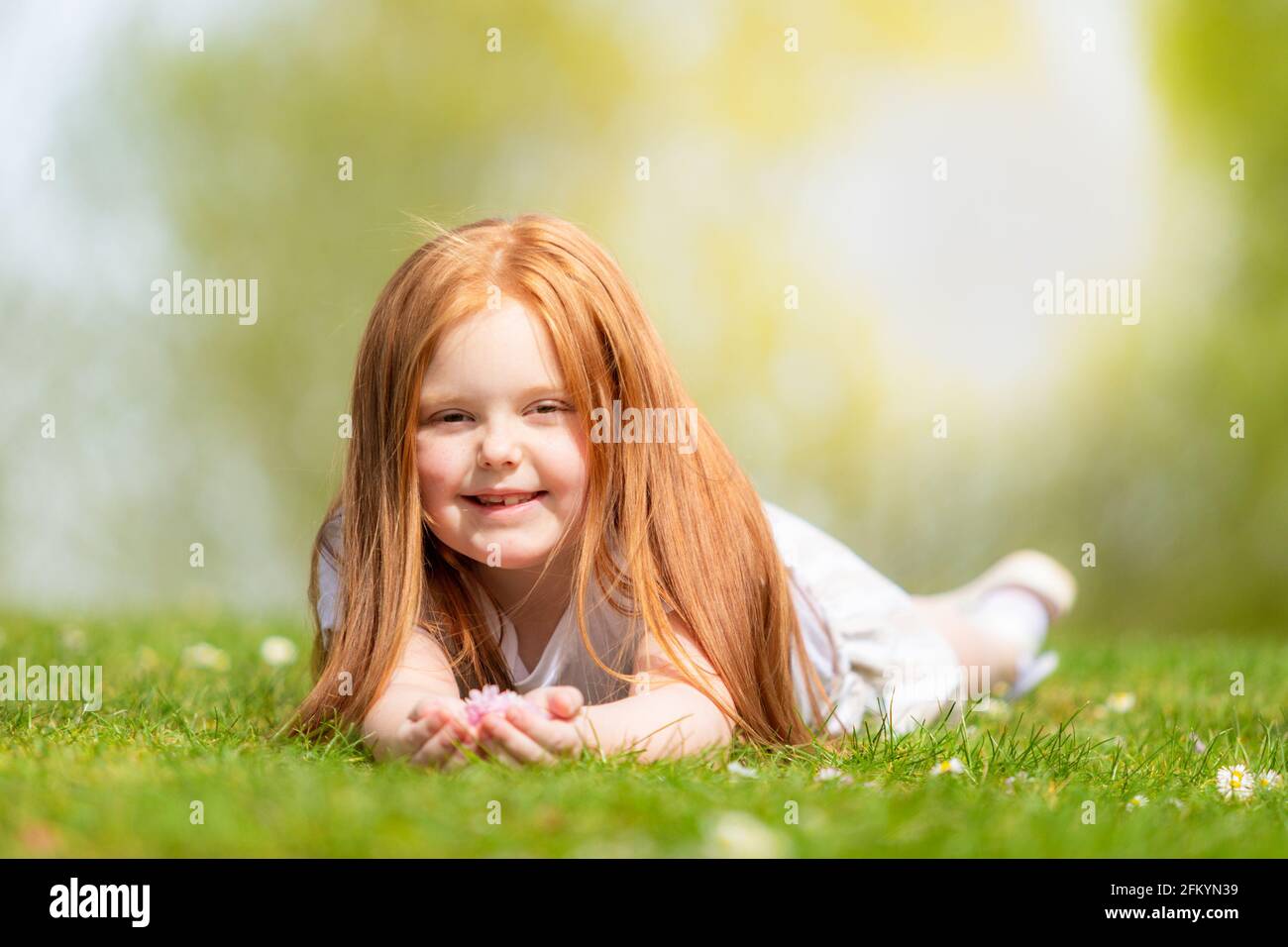 Sechs Jahre altes Mädchen, das draußen auf dem Gras liegt und lächelt Stockfoto