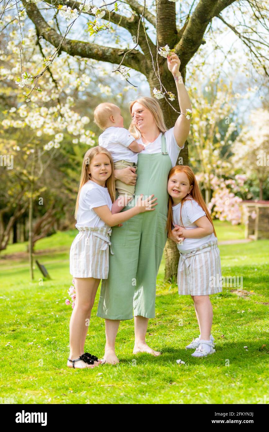 Schwangerschaftsmutter mit ihren zwei jungen Töchtern und ihrem kleinen Sohn Draußen in einem öffentlichen Park Stockfoto