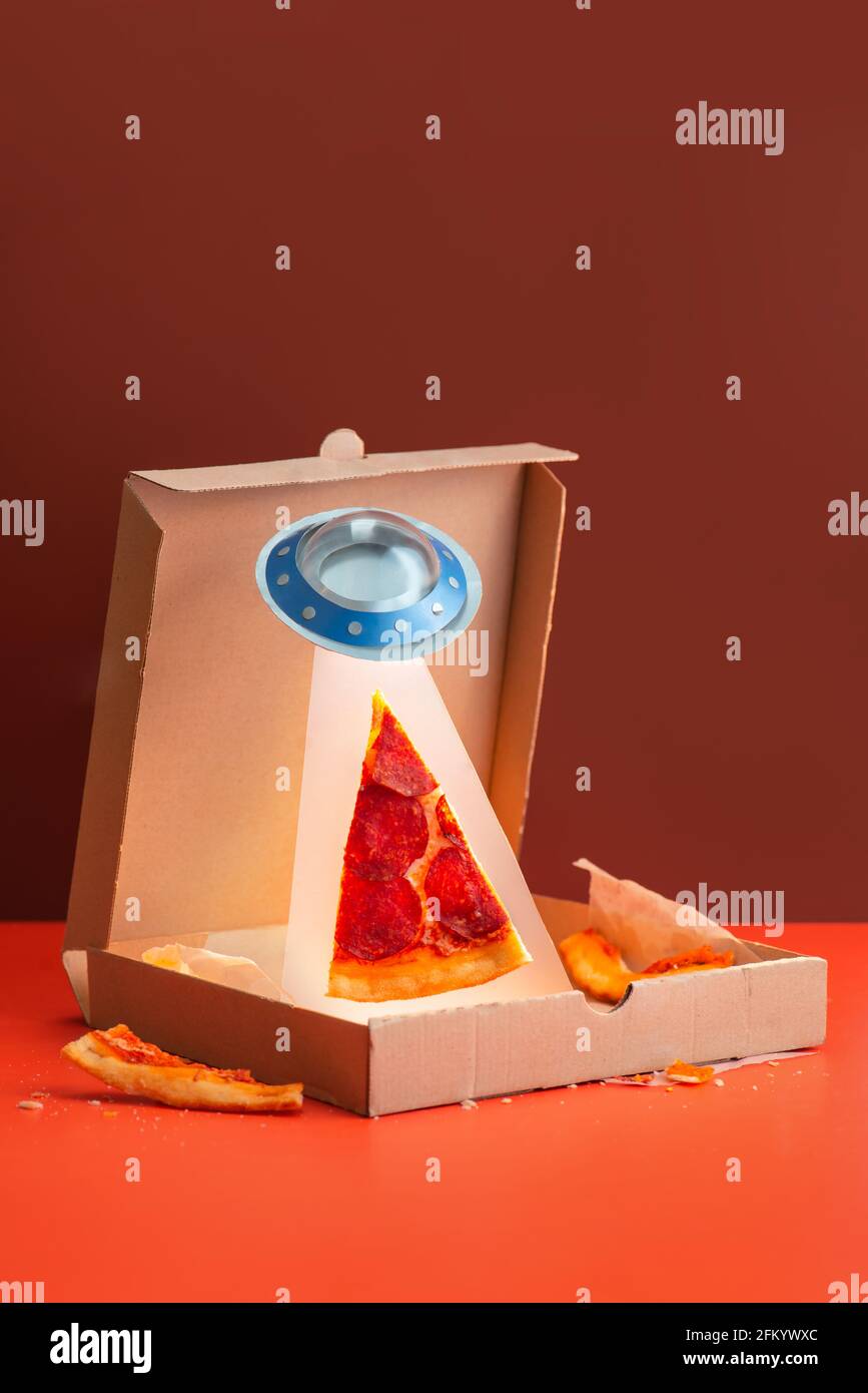 UFO stiehlt eine Pizzascheibe aus einer Schachtel, kreative Food-Fotografie in Rottönen, lustige Idee Stockfoto