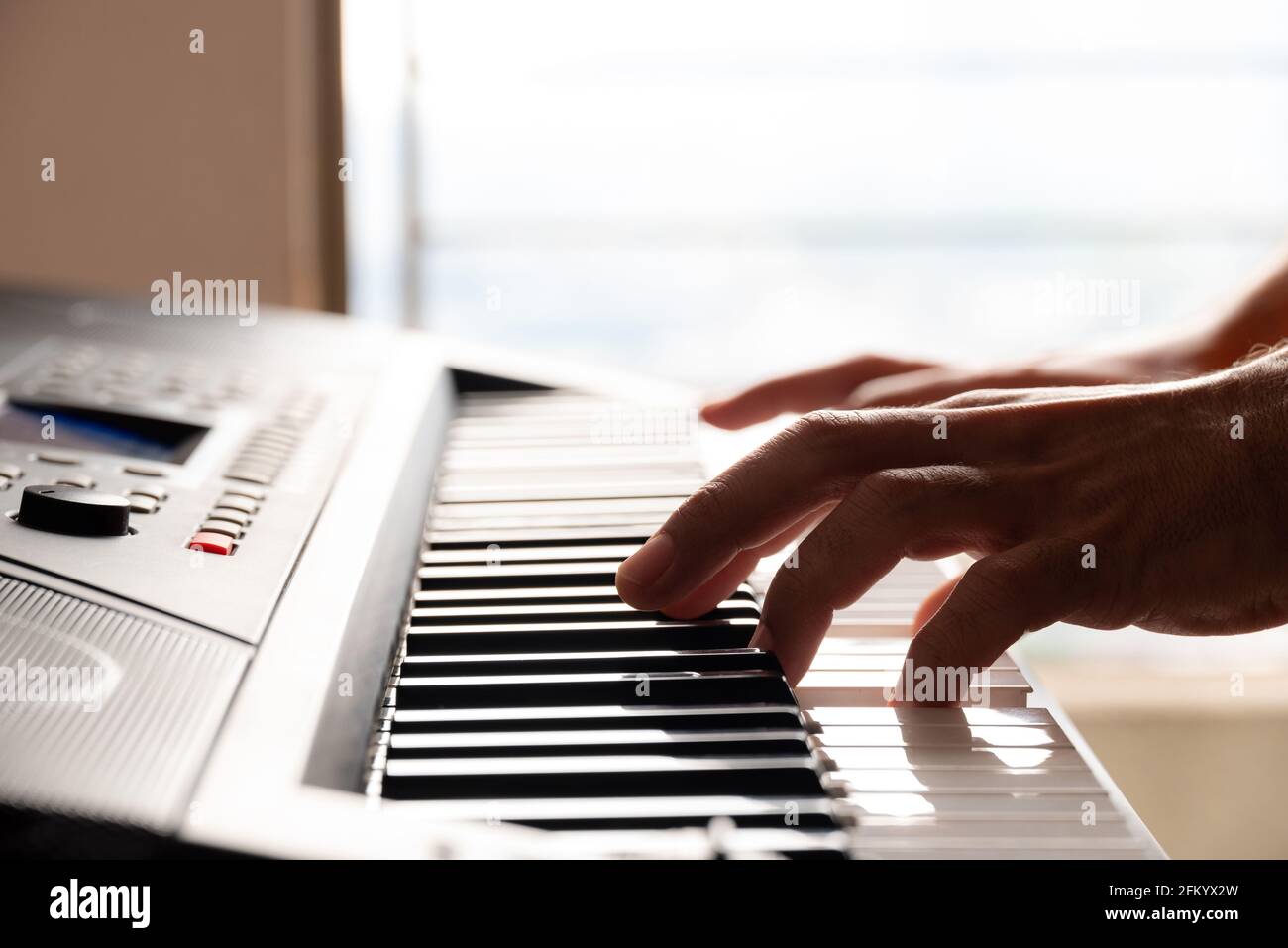 Nahaufnahme eines jungen Mannes, der zu Hause Klavier spielt Mit Fensterbeleuchtung Stockfoto