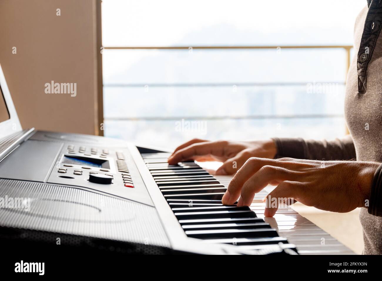Nahaufnahme eines jungen Mannes, der zu Hause Klavier spielt Mit Fensterbeleuchtung Stockfoto