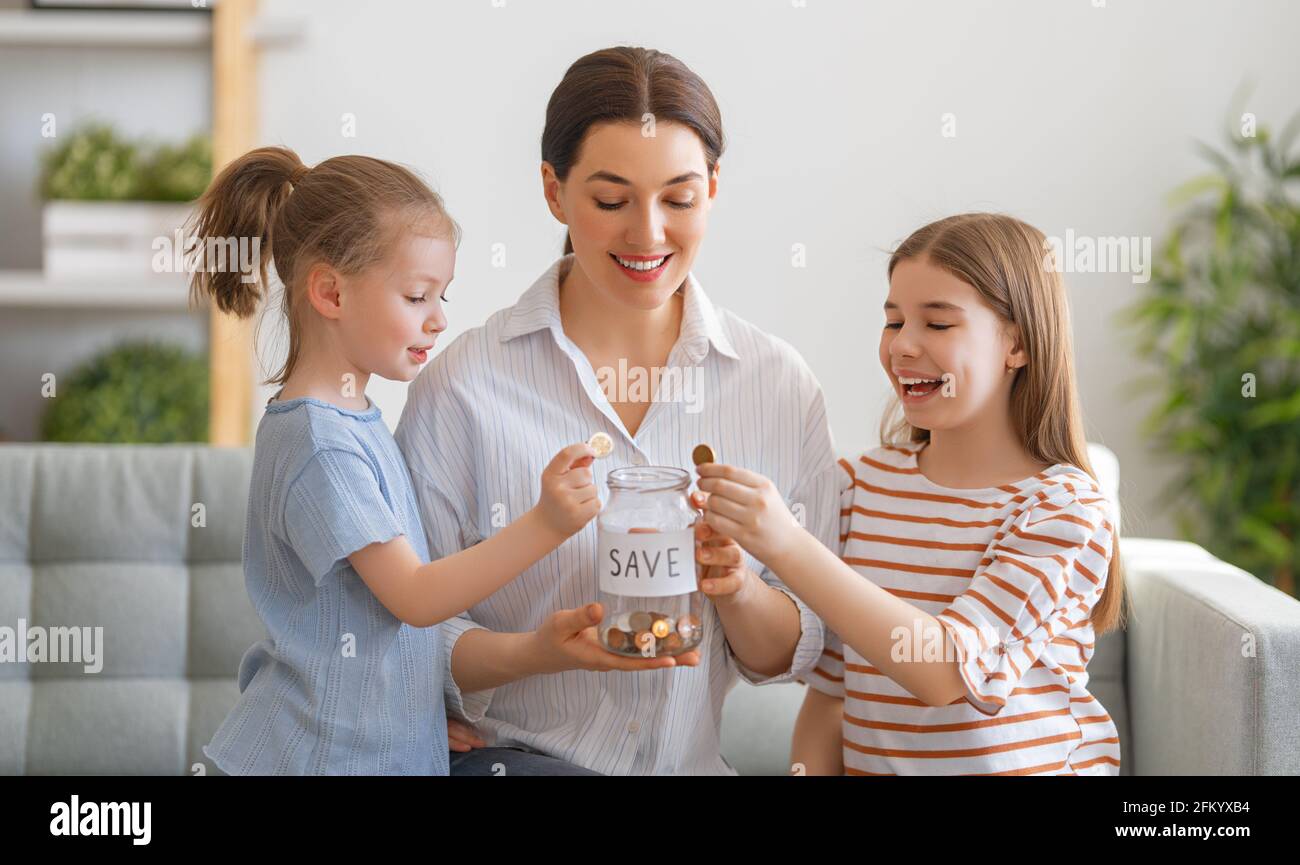 Mutter und Töchter halten Geldkasten, Mädchen setzen Münze. Geldkasten, Mädchen setzen Münze. Stockfoto