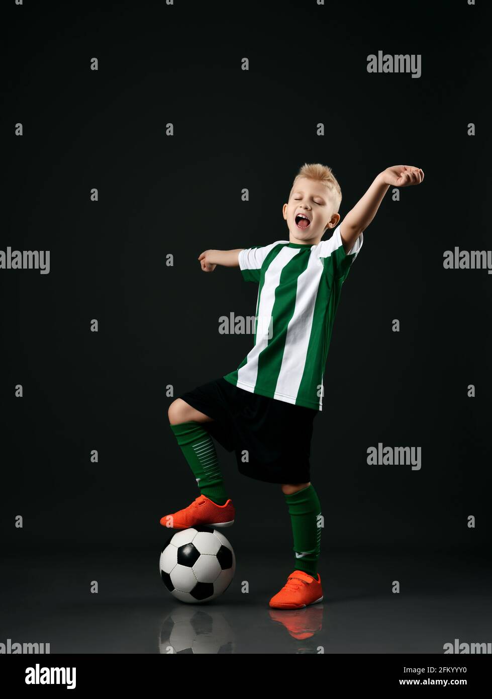 Fußballschüler, Junge in rot-weißer Uniform, steht mit Ball unter dem Fuß und hält die Arme ausgestreckt Stockfoto
